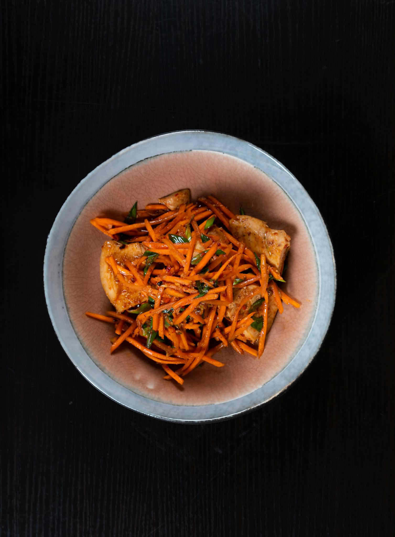 A bird's-eye view of a gourmet carrot and potato dish with herbs, served in a rustic bowl on a dark wooden table.