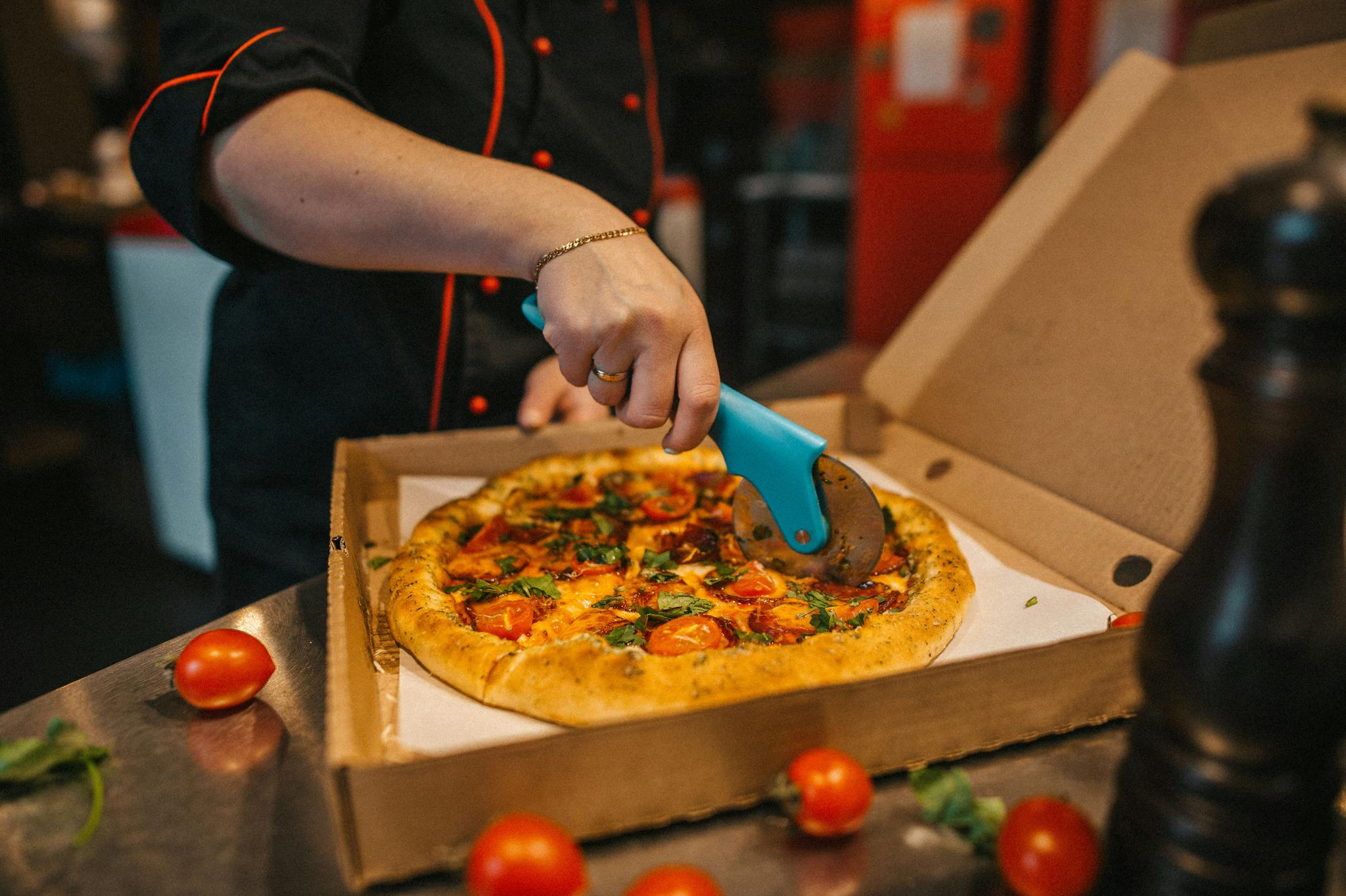 Close-up of a chef slicing a freshly baked pizza with a cutter in a kitchen. Vibrant ingredients on a rustic crust.