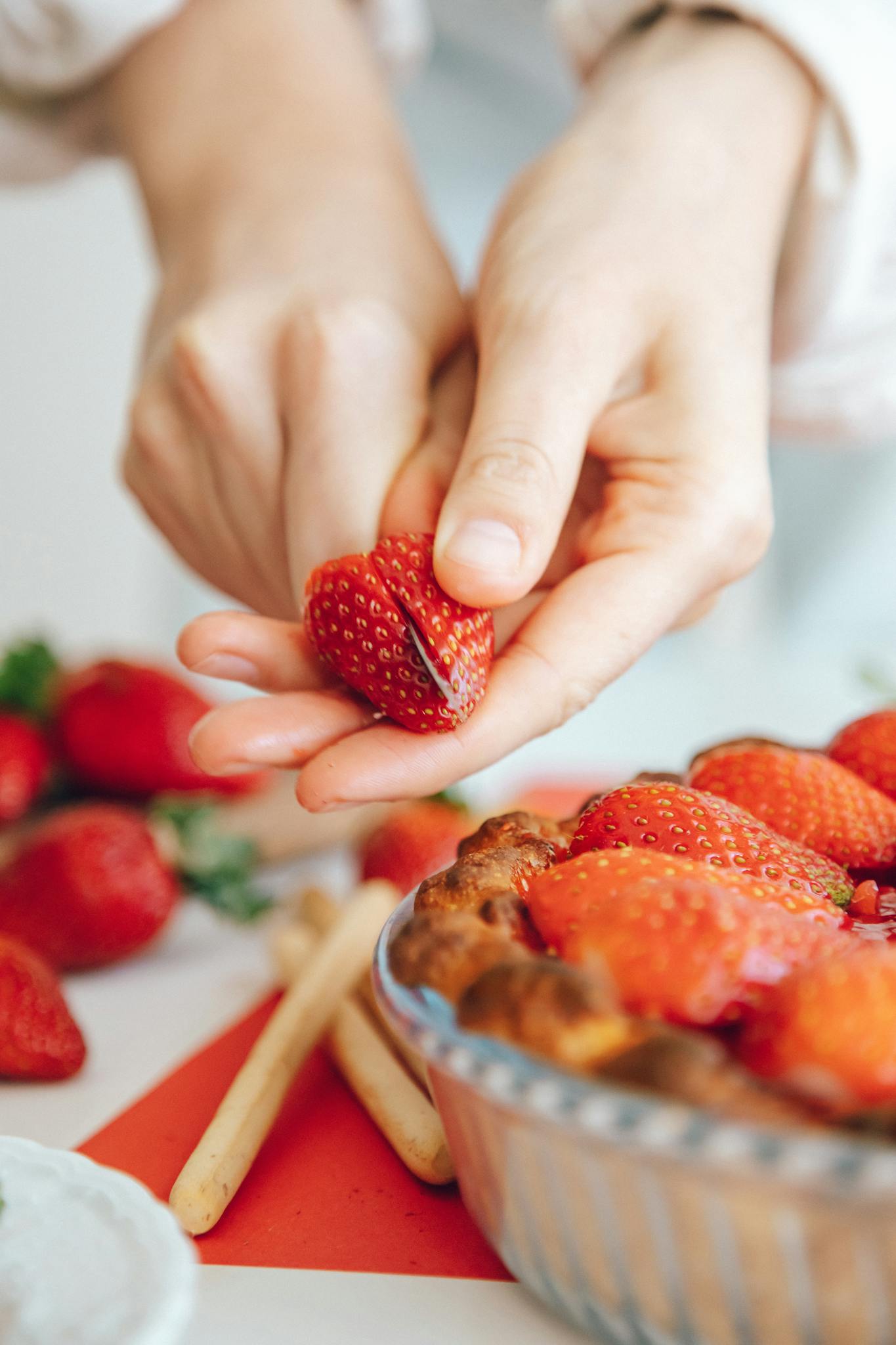 Hands slicing fresh strawberries to garnish a homemade pie.